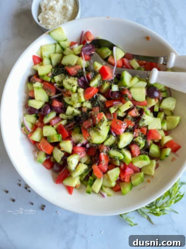Hellenic Cucumber Medley 7 Vinaigrette being carefully poured over the fresh mixture of cucumbers, tomatoes, and red onion in a white bowl.