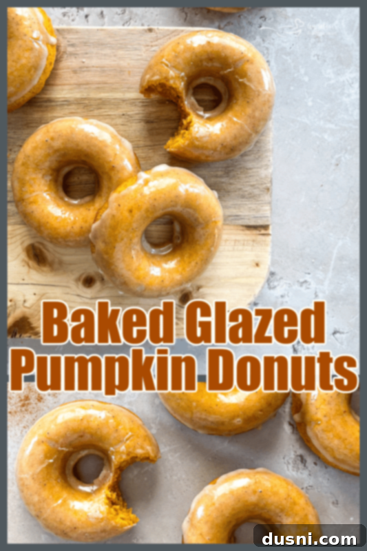 A stack of beautifully Glazed Baked Pumpkin Donuts on a fall-themed background.