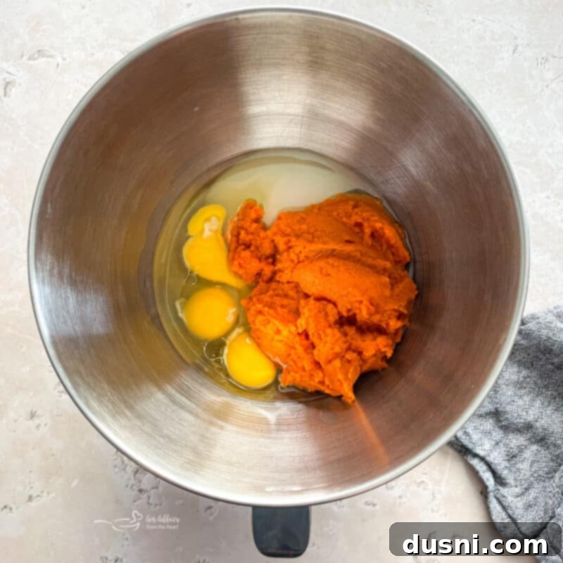 Mixing pumpkin, oil, eggs, and sugar in a stand mixer bowl for donut batter.