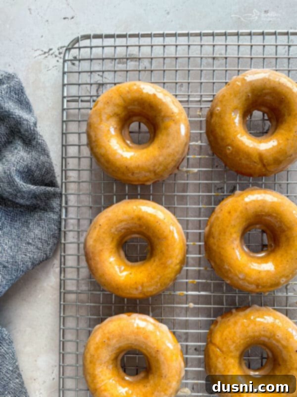 Warm Glazed Baked Pumpkin Donuts cooling on a wire rack after being dipped in spiced glaze.