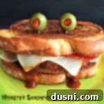 Epic Pizza Sandwiches 11 Close up of a Pizza Monster Sandwich on a green plate, highlighting the melted cheese fangs and olive eyes.