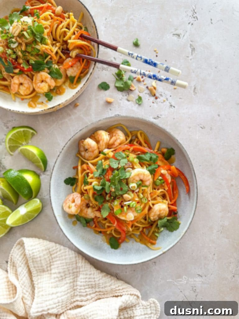 A large pot filled with noodles, vegetables, and shrimp in a rich Pad Thai sauce, simmering on a stovetop.