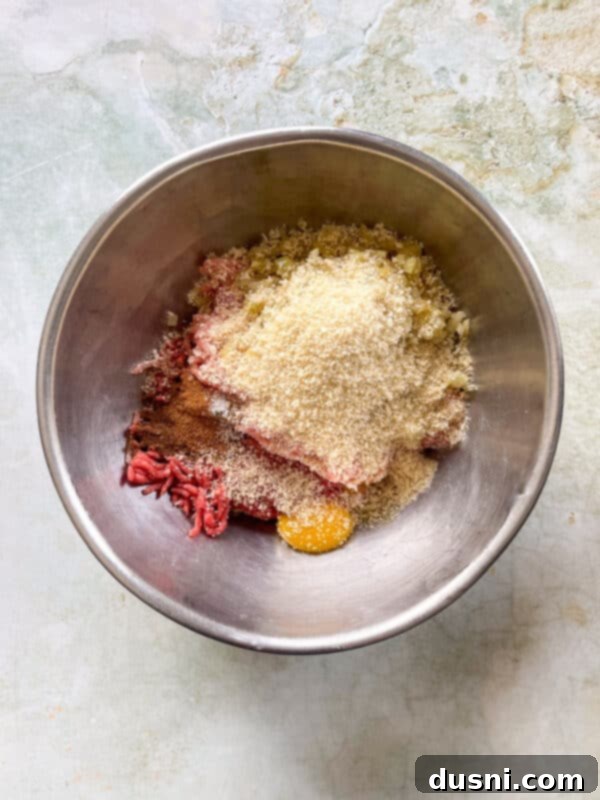 Mixing bowl with ground beef, ground pork, panko, egg yolks, and spices ready to be combined for meatballs