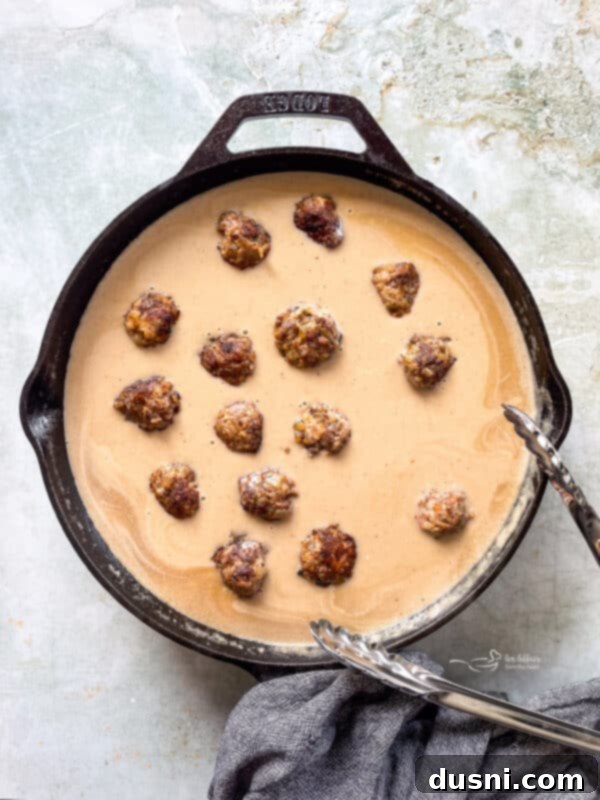 A close-up of a skillet filled with fully cooked Swedish meatballs simmering in a creamy gravy, ready to be served