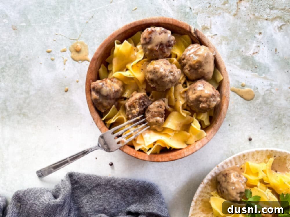 A serving of Swedish meatballs on a bed of egg noodles, garnished with fresh parsley