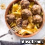 Swedish meatballs and egg noodles in a wooden bowl, up close, garnished with fresh herbs