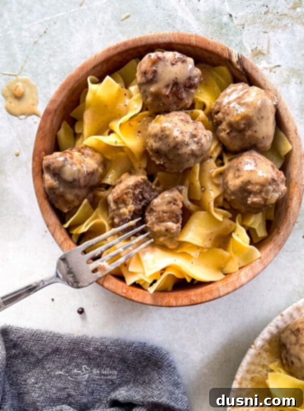 A wooden bowl filled with creamy Swedish meatballs and egg noodles, seen from above