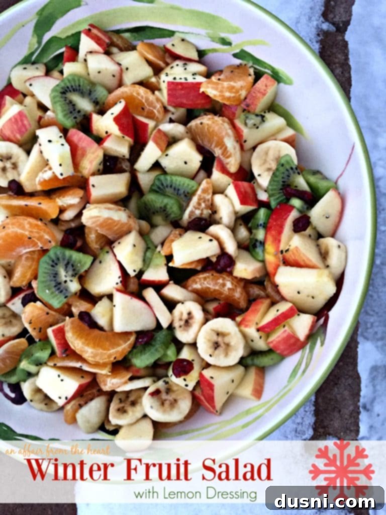 A vibrant bowl of Winter Fruit Salad with Lemon Dressing, featuring diced apples, segmented mandarins, sliced kiwis, bananas, and craisins, ready to be served.