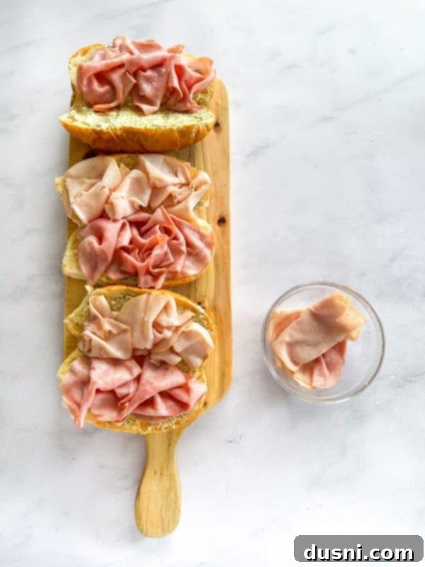 Turkey and ham slices being layered onto the hoagie roll.
