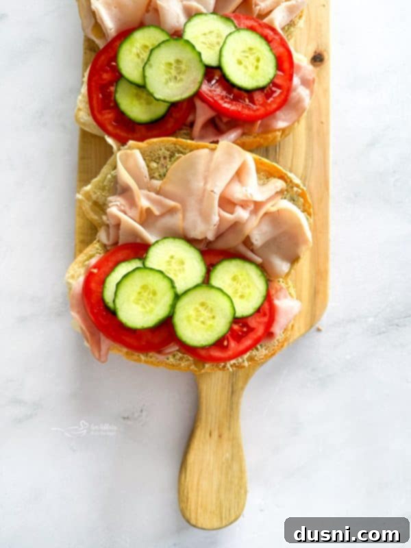 Cucumber and tomato slices being added over the meats.