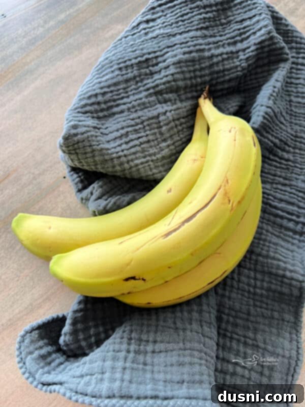 Three ripe bananas on a wooden cutting board, with one being peeled.