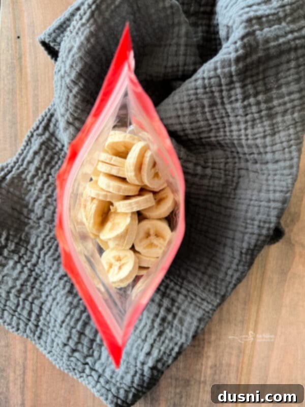 Sliced bananas arranged on a parchment-lined baking sheet for single-layer freezing.