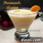 Orange Cream Dream Martini 2 Dreamsicle martini in a martini glass garnished with an orange slice on a white surface. Text "dreamsicle martini"