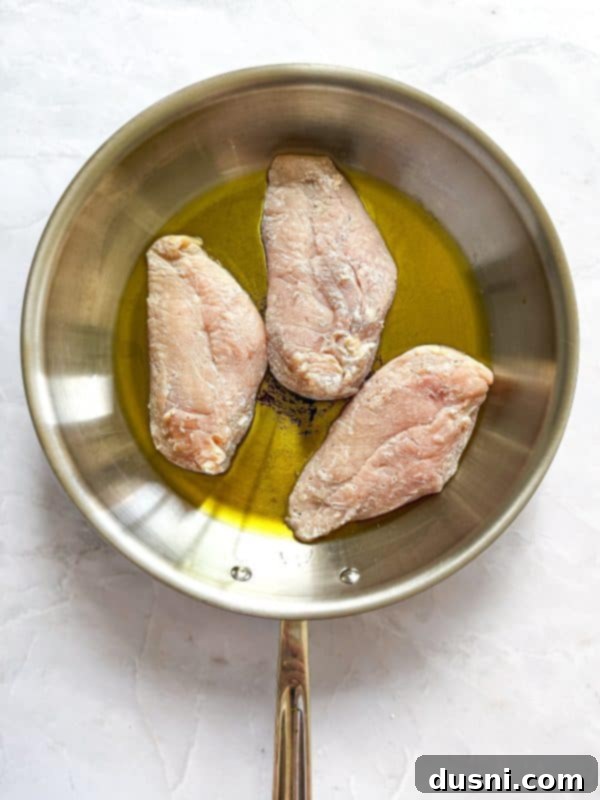 Creamy Chicken and Mushroom Florentine Pasta 10 Chicken breasts searing in a large skillet, developing a golden-brown crust.