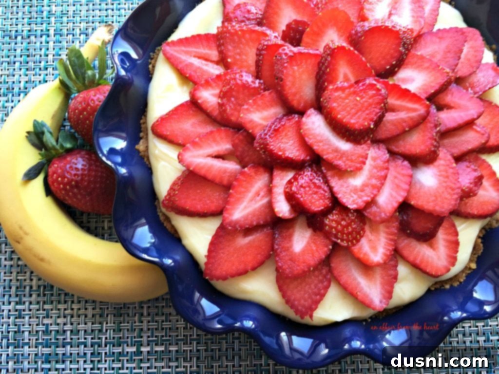 A vibrant Strawberry Banana Cream Pie with fresh strawberries arranged in a spoke pattern on top of creamy vanilla custard and banana slices, all encased in a graham cracker crust.