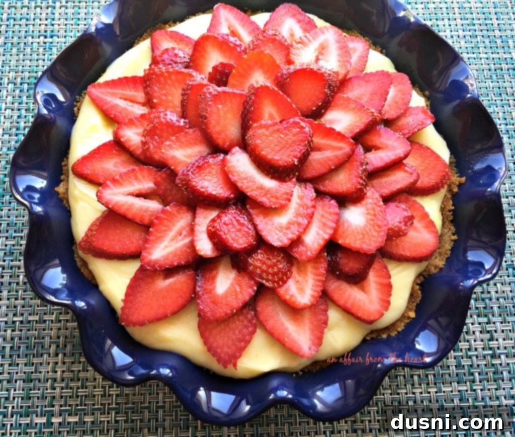 Close-up of a slice of Strawberry Banana Cream Pie, showing the layers of graham cracker crust, vanilla custard, banana, and fresh strawberry topping.