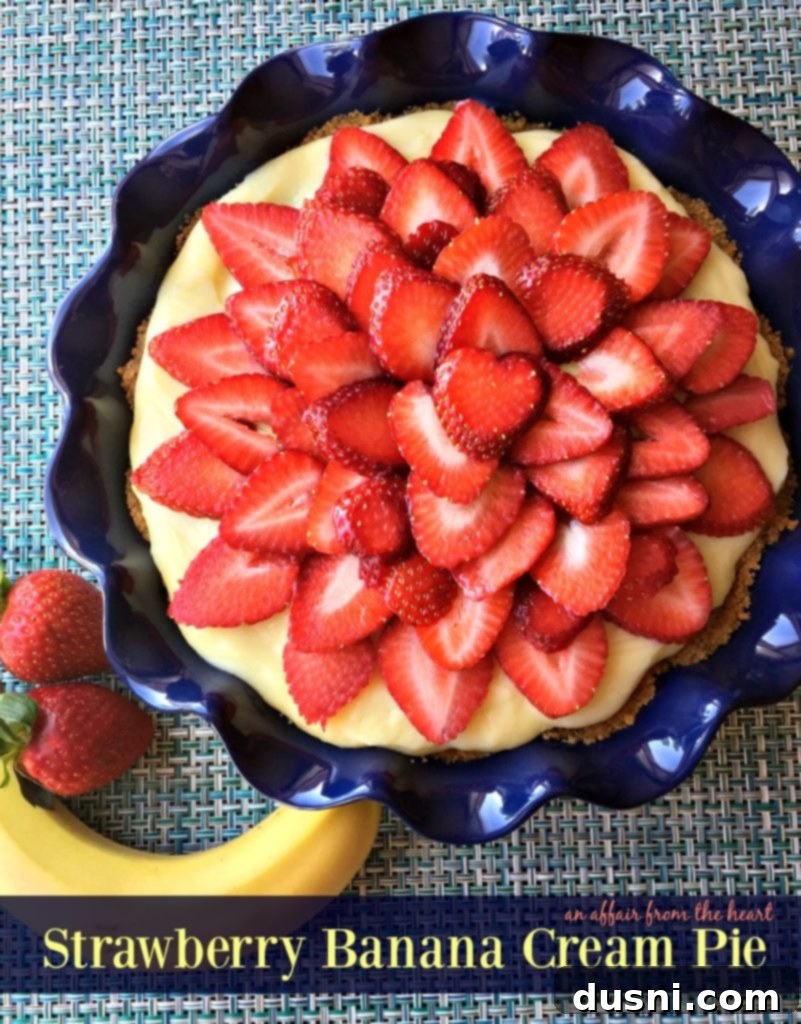A close-up, top-down shot of a Strawberry Banana Cream Pie, featuring a heart-shaped strawberry in the center and other strawberry slices arranged around it, highlighting the beautiful presentation.