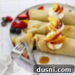 Golden Crepes Topped with Summer Fruits 17 Using a fork and knife to take a bite out of a sweet crepe with summer fruit.