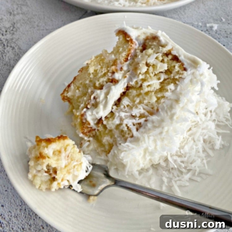 Ultimate Chocolate Pudding Dream Cake 18 A fork with a bite of the COCONUT CREAM POKE CAKE WITH COCONUT WHIPPED CREAM FROSTING next to the slice of cake on a white plate