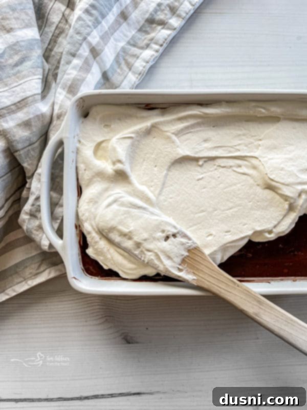Ultimate Chocolate Pudding Dream Cake 9 Spreading whipped cream evenly over the chocolate pudding layer on the poke cake.