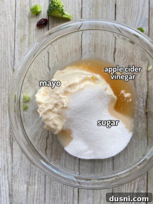 Smoky Cashew Broccoli Crunch 5 Top view of three small bowls on a wooden surface, containing mayonnaise, granulated sugar, and apple cider vinegar—ingredients for the salad dressing.