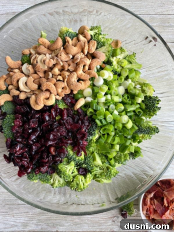 Smoky Cashew Broccoli Crunch 6 One large bowl filled with fresh broccoli florets, cashews, sliced green onions, and Craisins, ready for dressing.