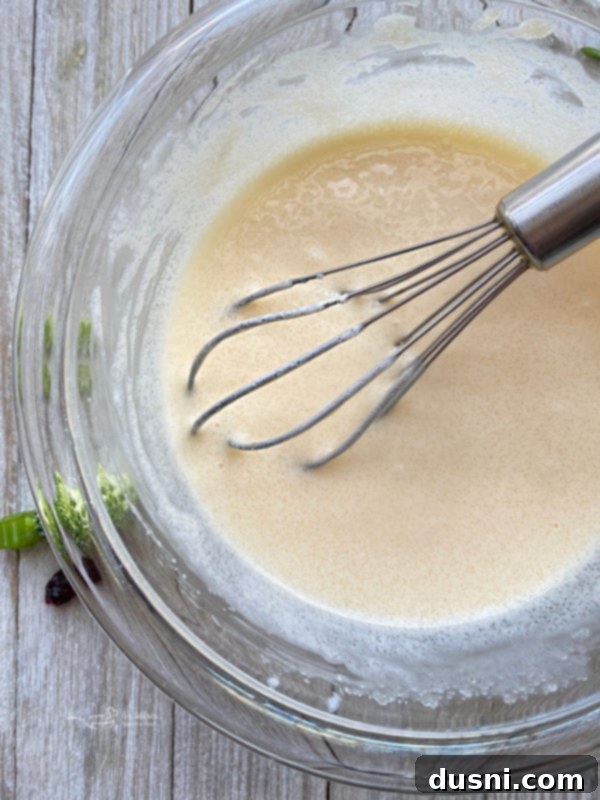 Smoky Cashew Broccoli Crunch 8 One small bowl containing the creamy dressing for bacon cashew broccoli salad, featuring mayonnaise, sugar, and apple cider vinegar thoroughly mixed.