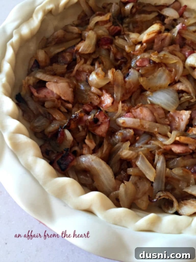 The savory onion and bacon filling neatly arranged in a pie crust, ready for the egg mixture