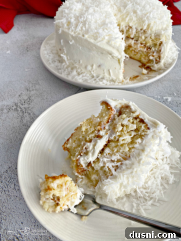A beautifully sliced coconut cream poke cake, showing the moist layers and fluffy frosting, garnished with toasted coconut flakes.