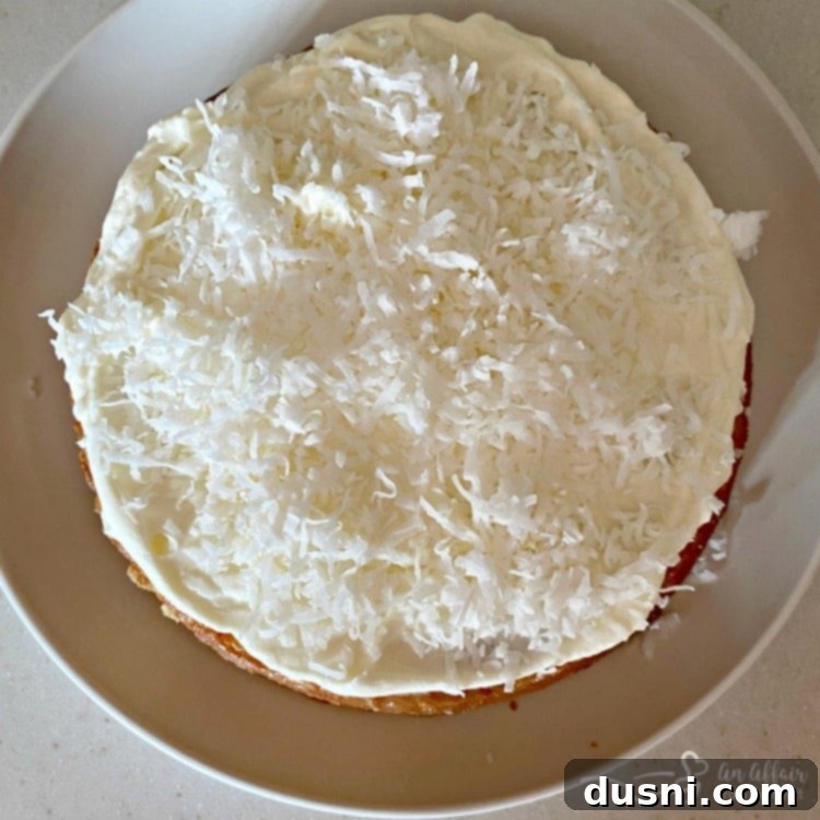 The process of layering the Coconut Cream Poke Cake, showing the bottom layer with frosting and coconut.