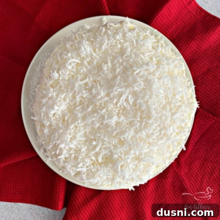 A completed Coconut Cream Poke Cake with Coconut Whipped Cream Frosting, garnished with shredded coconut.