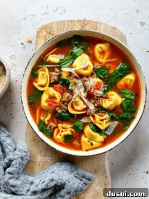 A bowl of Tortellini soup with sausage and spinach.
