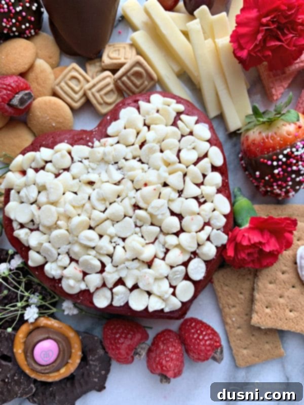 A stunning Valentine's Dessert Cheese Board featuring a heart-shaped red velvet cheese ball, fresh berries, chocolates, and crackers, perfect for a romantic spread.