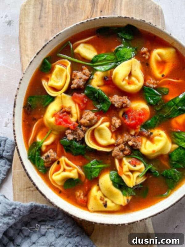 Close-up of a spoon dipping into a bowl of tortellini soup with sausage and spinach