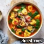 Close up of Tortellini soup with sausage in a white bowl.