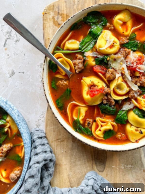 Overhead shot of a bowl of cheesy tortellini soup with sausage, a spoon resting in it
