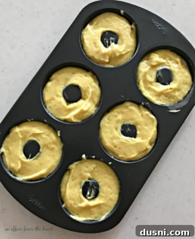 Close-up of a hand dipping a baked lemon donut into a bowl of lemon glaze