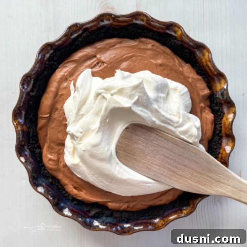 Spreading freshly whipped cream delicately over the chilled chocolate French Silk Pie filling.