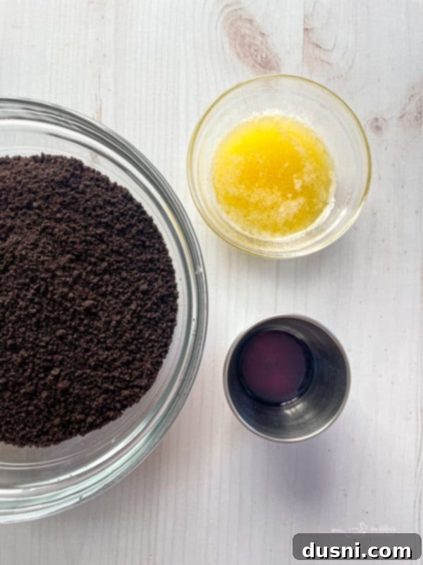 Ingredients for Oreo crust: Oreo crumbs, softened butter, and vanilla extract in small bowls.