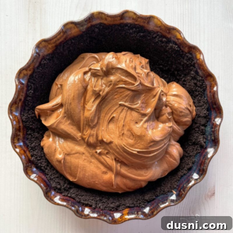 Smooth chocolate filling spread evenly over the baked Oreo crust in a pie pan.