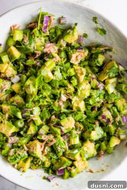 Creamy Avocado Tuna Bliss 3 Close-up of Avocado Tuna Salad in a white bowl with a fork, ready to be eaten.