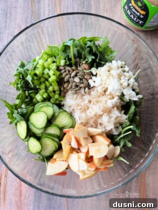 Viral Zest: Arugula Sauerkraut Salad 8 Adding cucumbers, apples, pepitas, and celery to a bowl of TikTok Sauerkraut Arugula Salad.