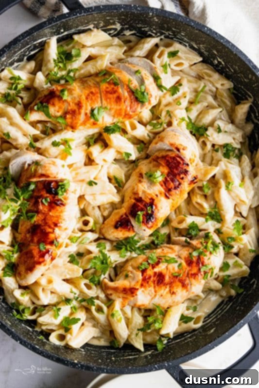A full skillet of Creamy Chicken Penne Pasta with sliced chicken and fresh parsley.
