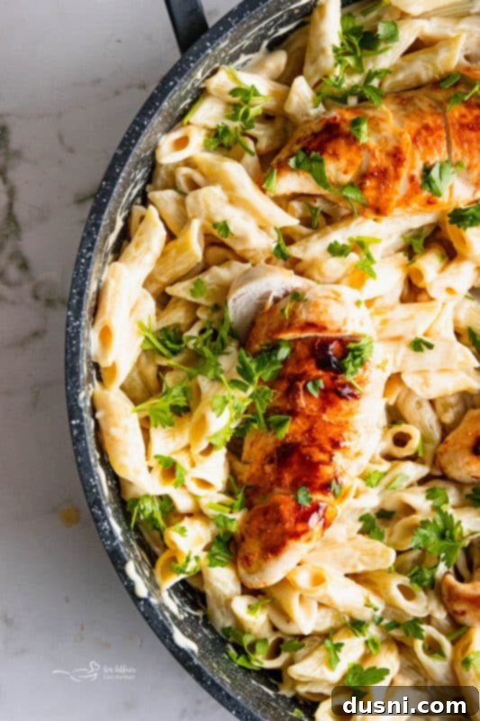 A wide shot of Creamy Chicken Penne Pasta in a black skillet, ready to be served, with a spoon in it.