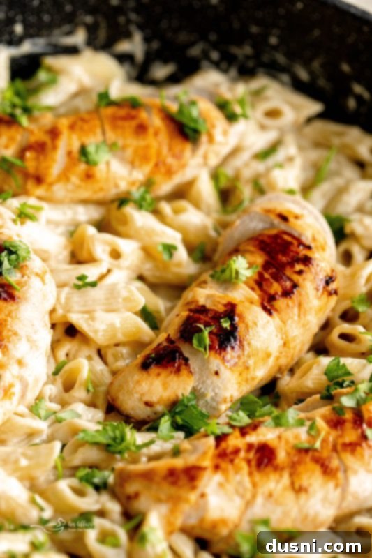 A close-up of a pan filled with creamy chicken penne pasta, with a serving spoon resting in it.