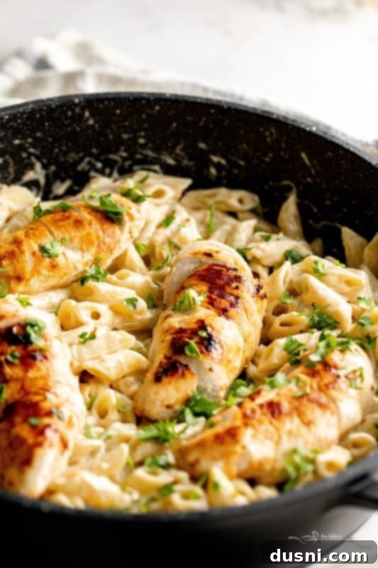 A wide shot of Creamy Chicken Penne Pasta in a black skillet, with a small bowl of fresh parsley on the side.