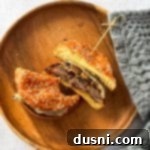 Signature Mushroom Swiss Burger 18 A mushroom Swiss burger cut in half on a wood plate. Half with a bite out of it, showcasing the melted cheese and mushrooms.