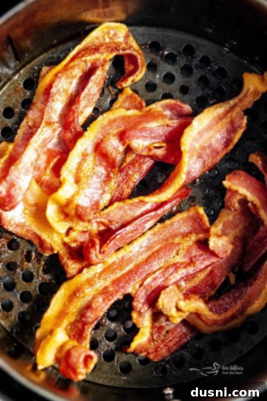 Perfectly Crispy Air Fryer Bacon 5 Air Fryer Bacon in a basket with tongs