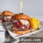 Pastrami Burger with Kraut on a white plate with corn and with burgers behind it