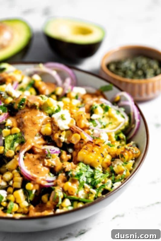 A serving of Grilled Corn and Avocado Salad on a white plate with fresh herbs